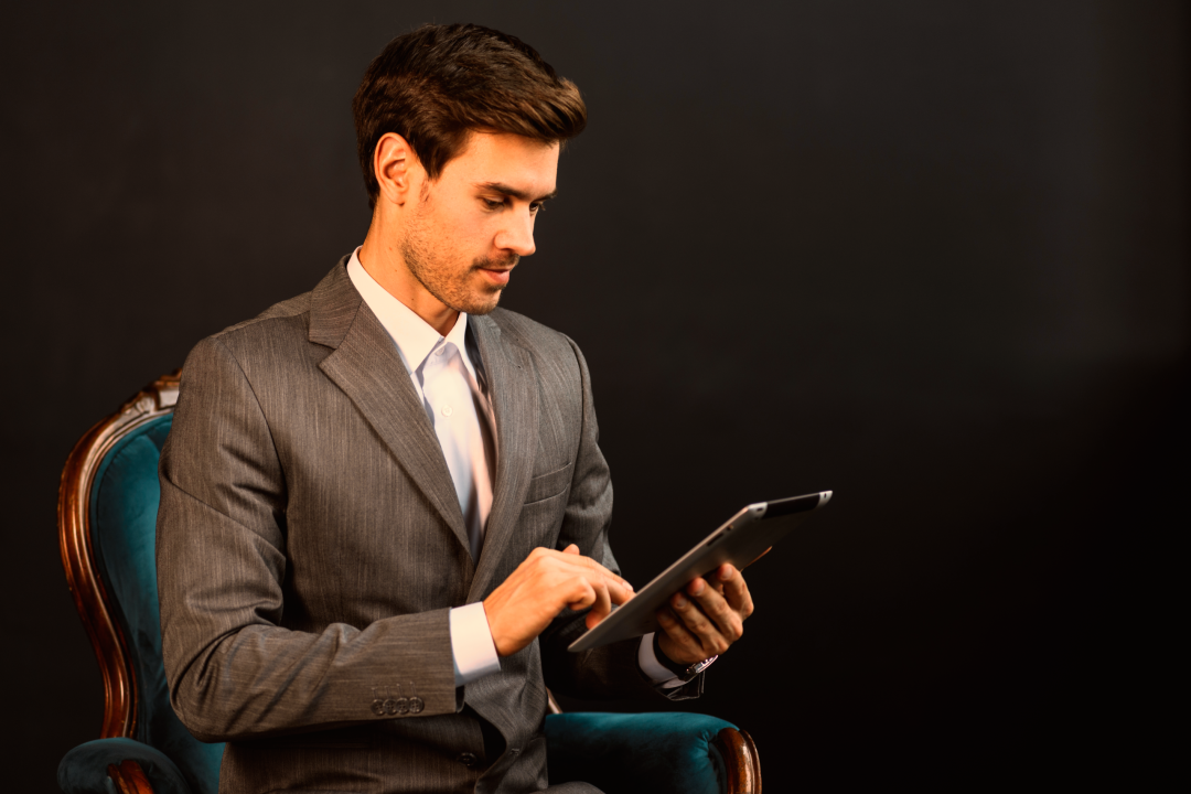 businessman-sitting-armchair-suit-using-digital-tablet-against-black-background